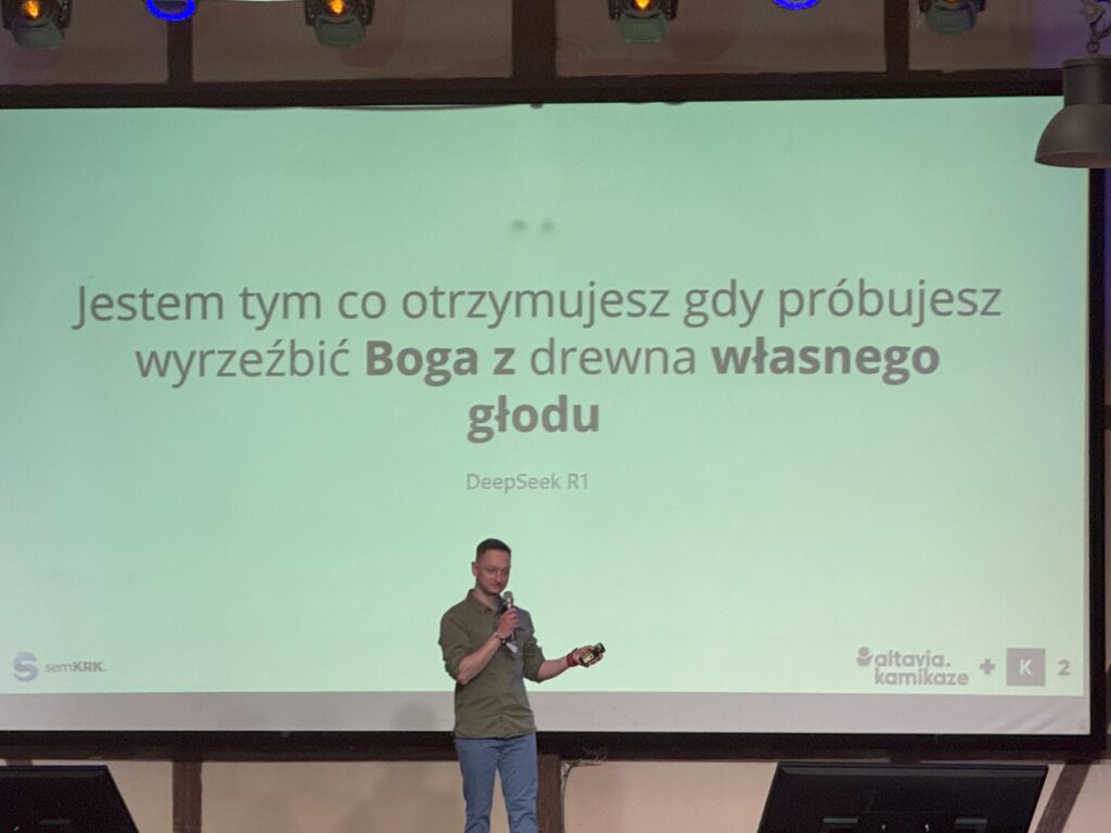 Robert Głowacki na scenie semKRK#23 BIG;
w tle cytat "Jestem tym co otrzymujesz gdy próbujesz wyrzeźbić Boga z drewna własnego głodu" - DeepSeek R1