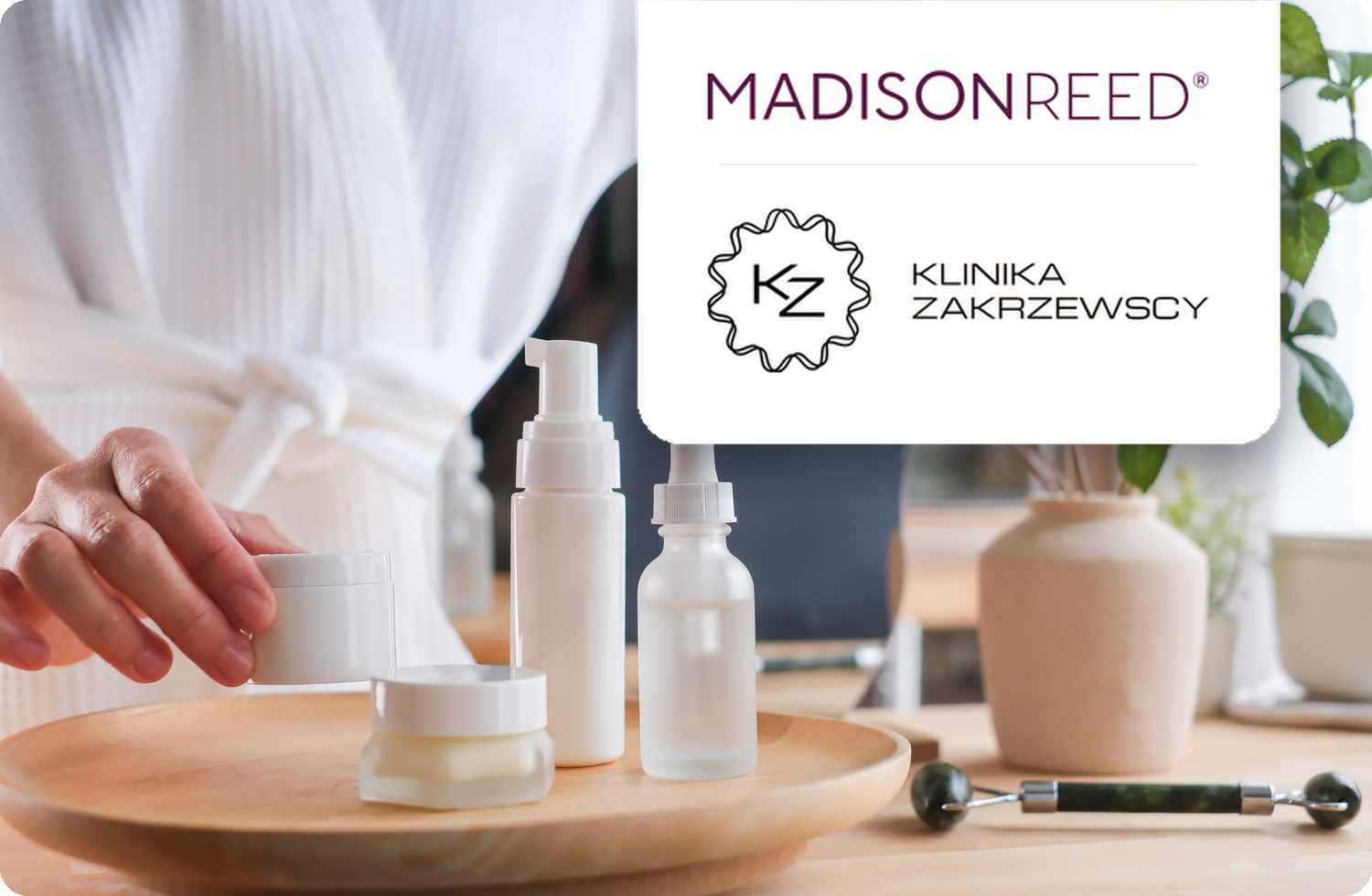 Kobieta w białym szlafroku układająca białe opakowania kosmetyków na drewnianej tacy. W prawym górnym rogu nałożone są logotypy marek: Madison Reed oraz Klinika Zakrzewscy.
